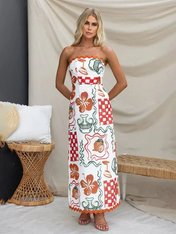 Strapless white maxi dress with an all-over orange, green, and red graphic print featuring fruits and vases.