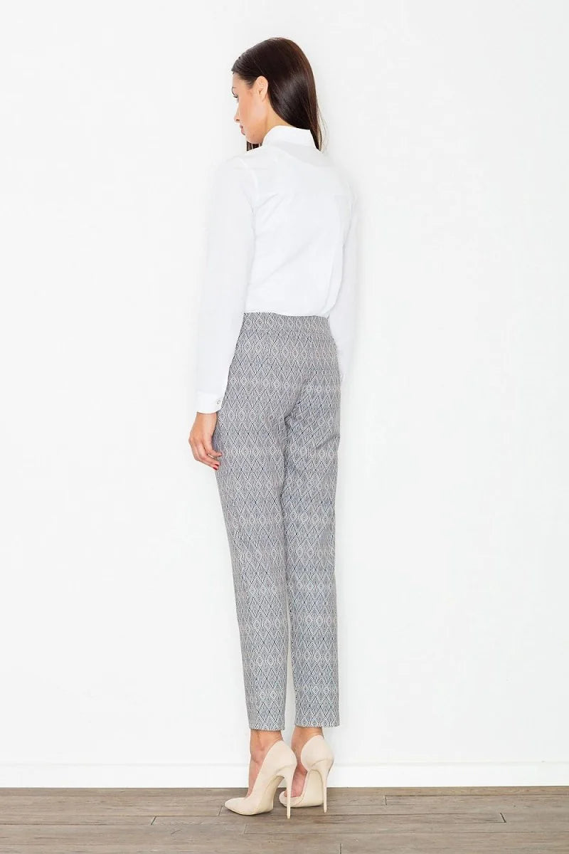 Woman wearing white shirt and grey printed pants with white heels, back view.