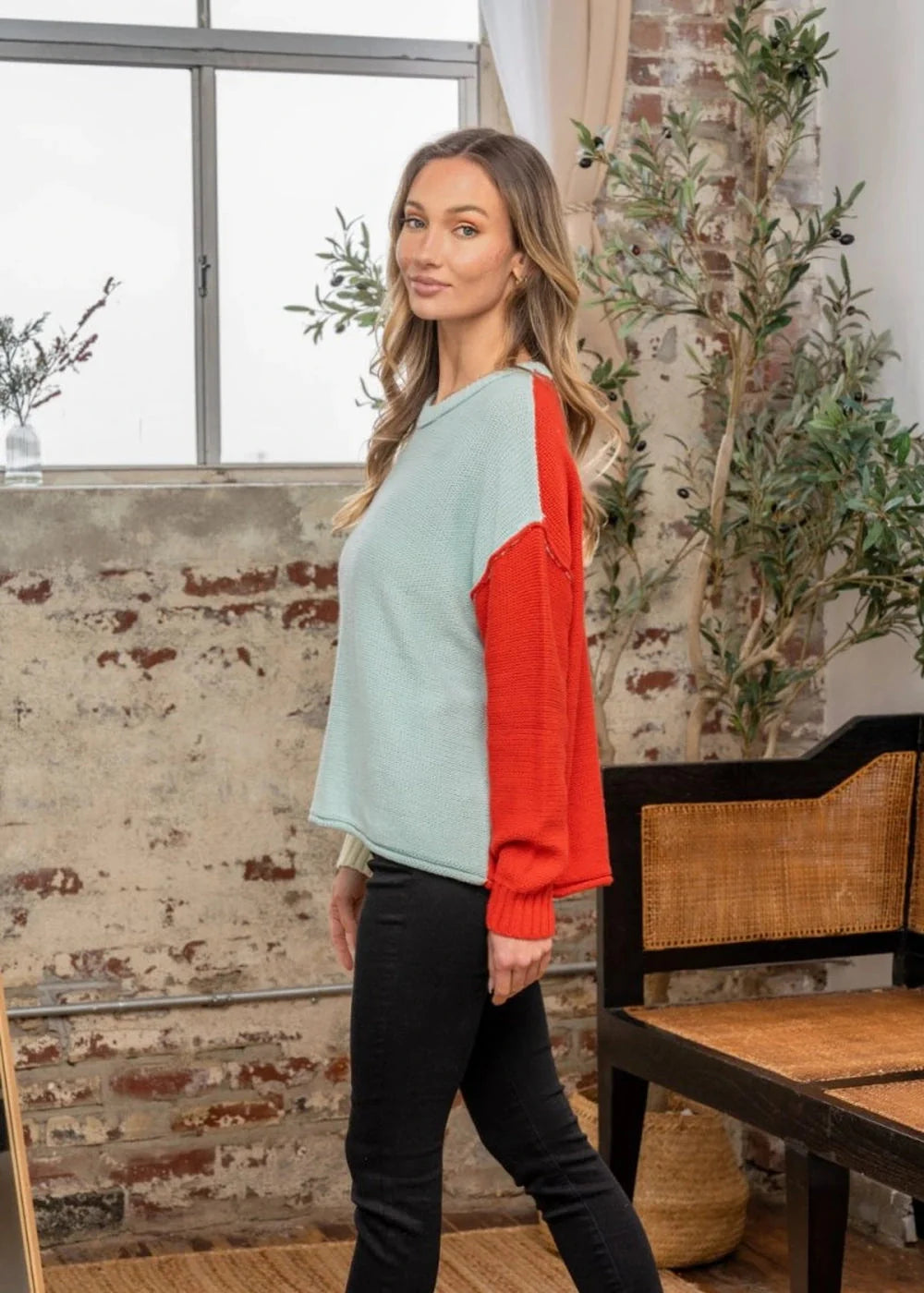 Relaxed fit sweater with a light blue body and bright orange sleeves, featuring a textured knit.