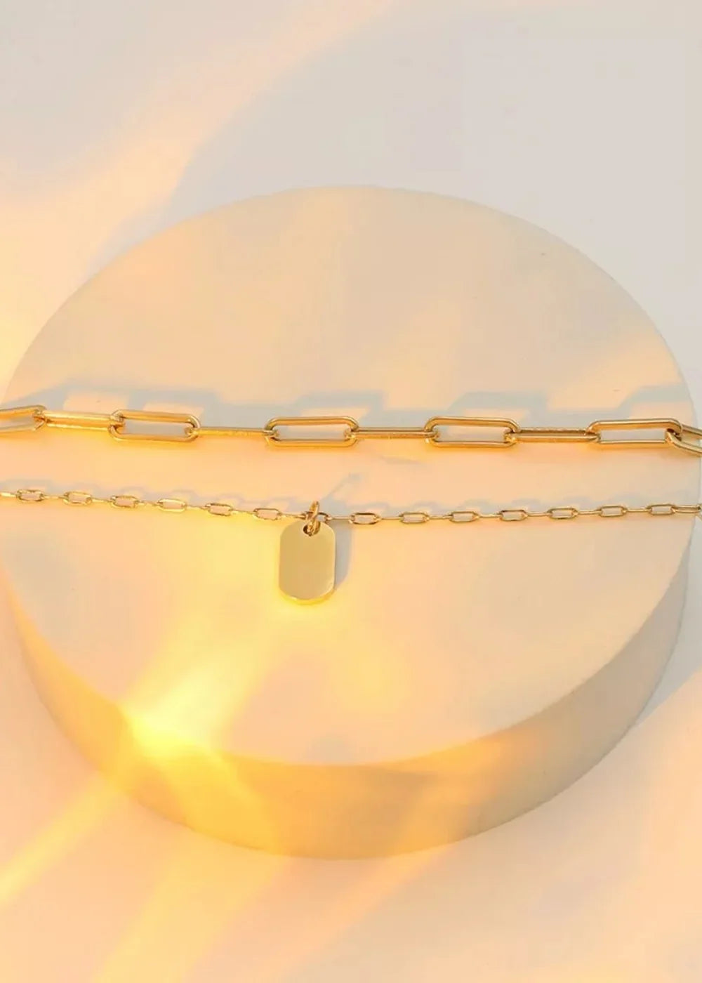 Gold-tone layered necklaces with a large paperclip chain and a smaller chain featuring a small rectangular tag.