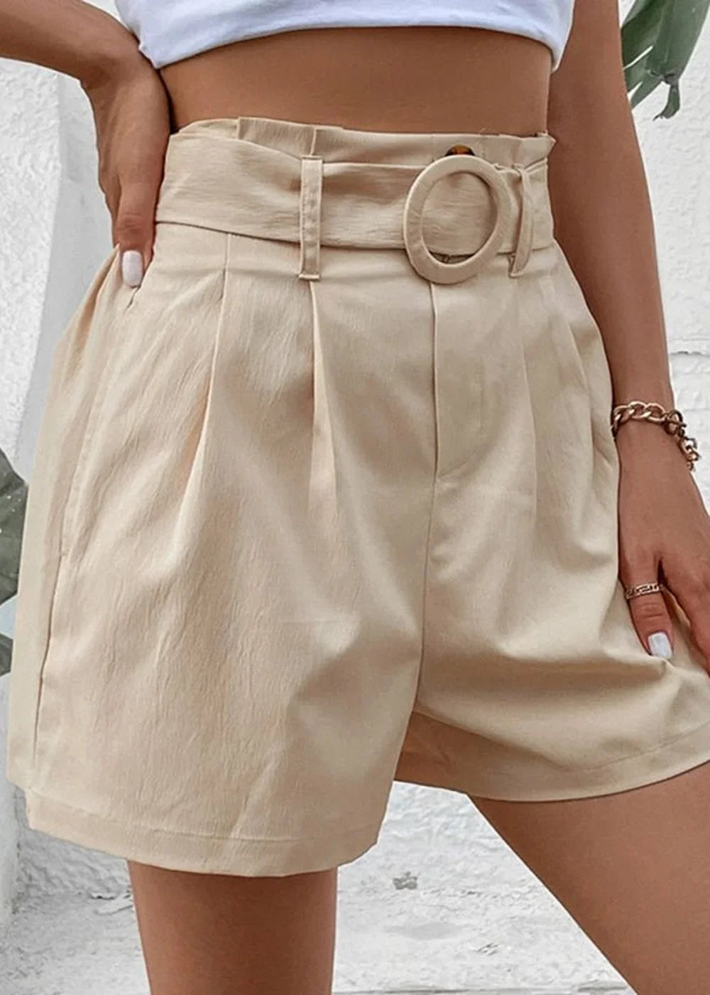 Light beige paperbag waist shorts with a belt and circular buckle detail, on model.