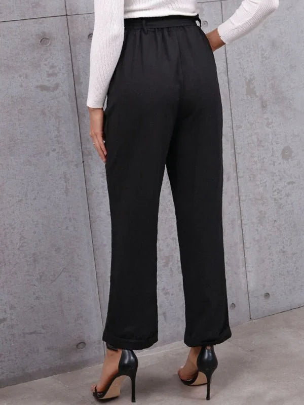 Black high-waisted pants with a tie waist, shown from the back on a model wearing black heels.