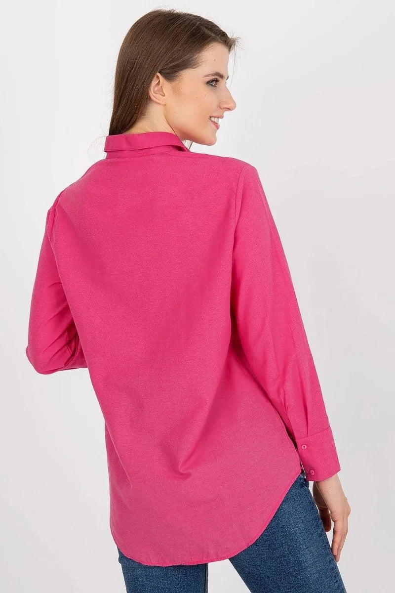 Back view of a woman wearing a loose-fit, bright pink collared shirt with long sleeves and button cuffs.