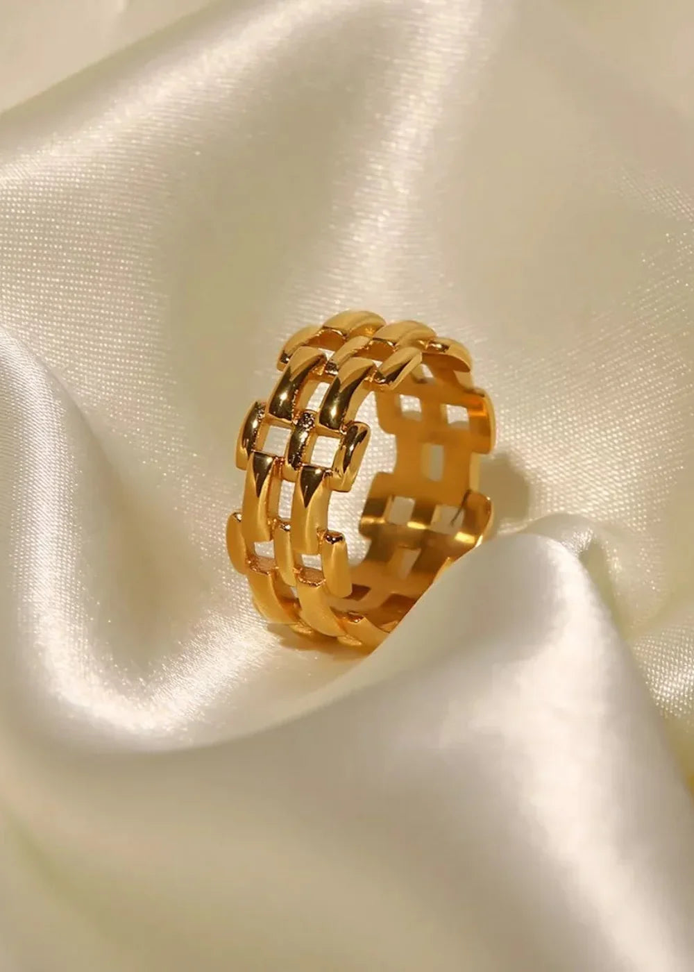 Gold-plated stainless steel ring with a geometric, interlocking link design on a satin white background.
