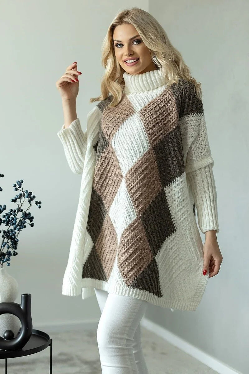 Woman in a white, brown, and tan argyle knit poncho sweater with a turtleneck and long sleeves, paired with white pants.