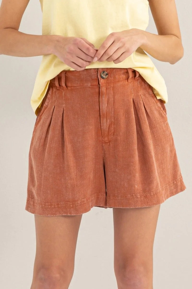 Terracotta linen-blend shorts with pleats and a button closure, on a model.