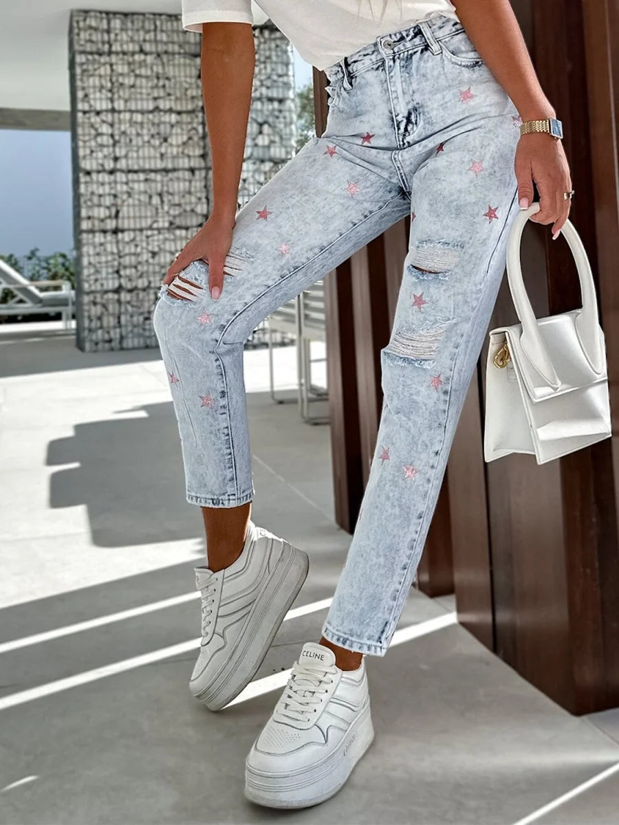 Light wash distressed denim jeans with pink star pattern and ripped knees.