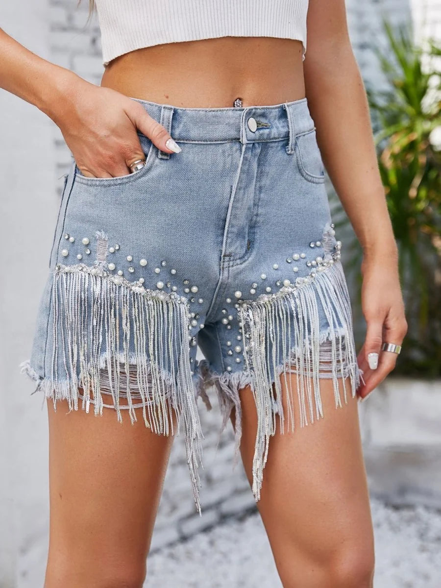 Light wash denim shorts with pearl and rhinestone embellishments and silver fringe detail.