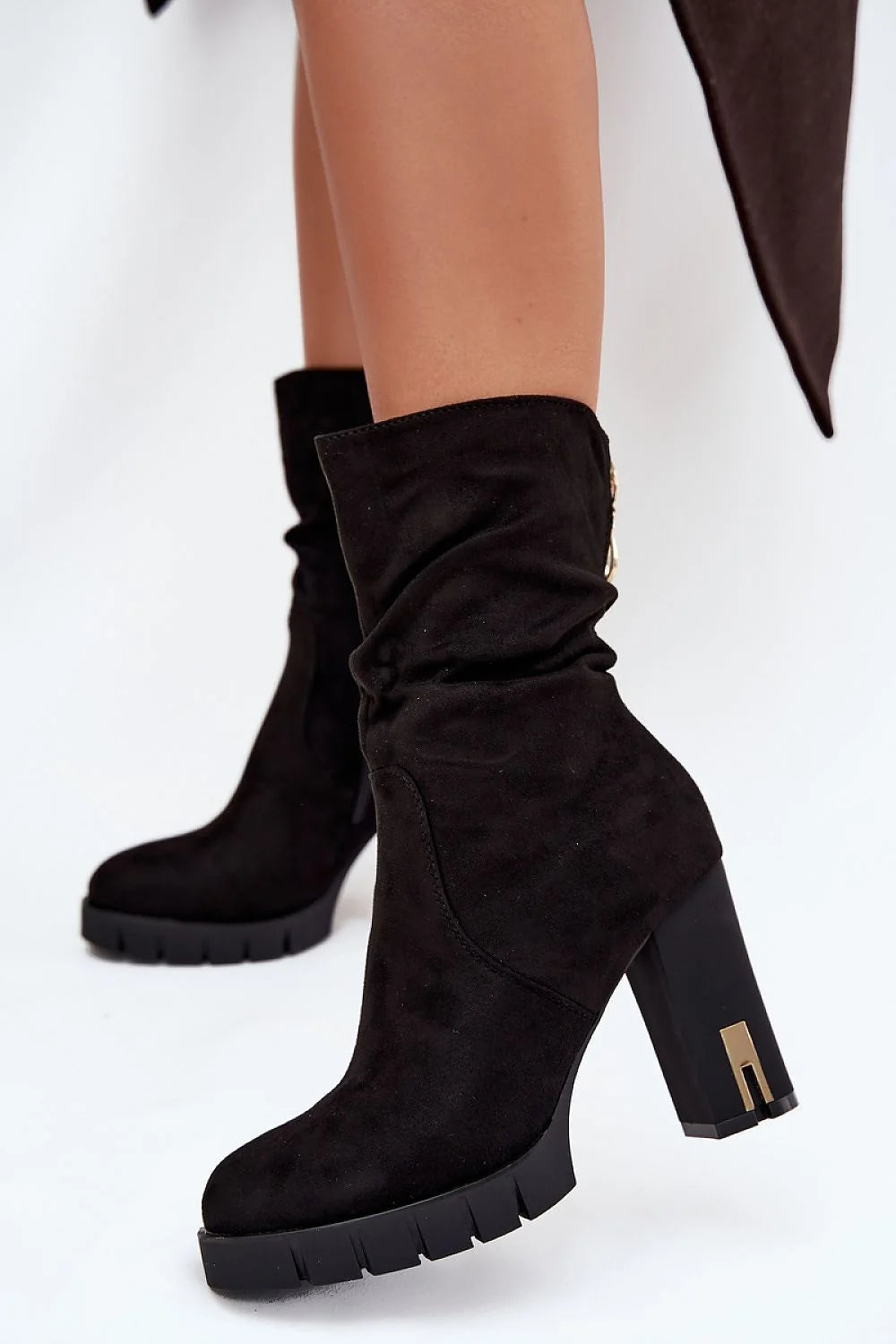 Black suede slouchy heeled boots with chunky platform sole and gold accent on heel.