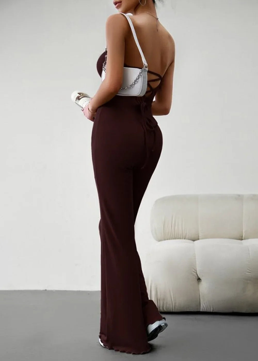 Brown wide-leg jumpsuit with lace-up back detail and white crossbody bag.