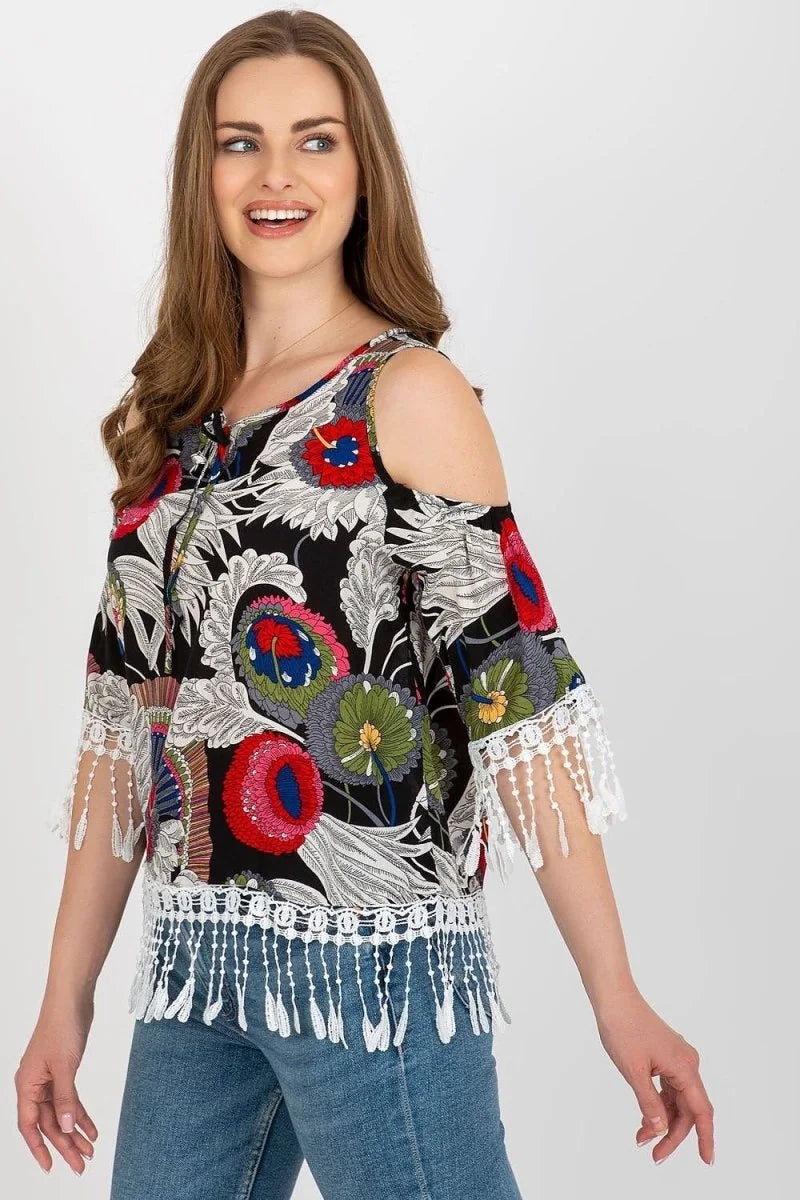 Black cold-shoulder top with colorful floral print, lace trim, and fringe detail.
