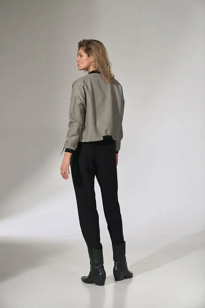 Woman in black pants and a grey and black patterned jacket with a black collar and cuffs.