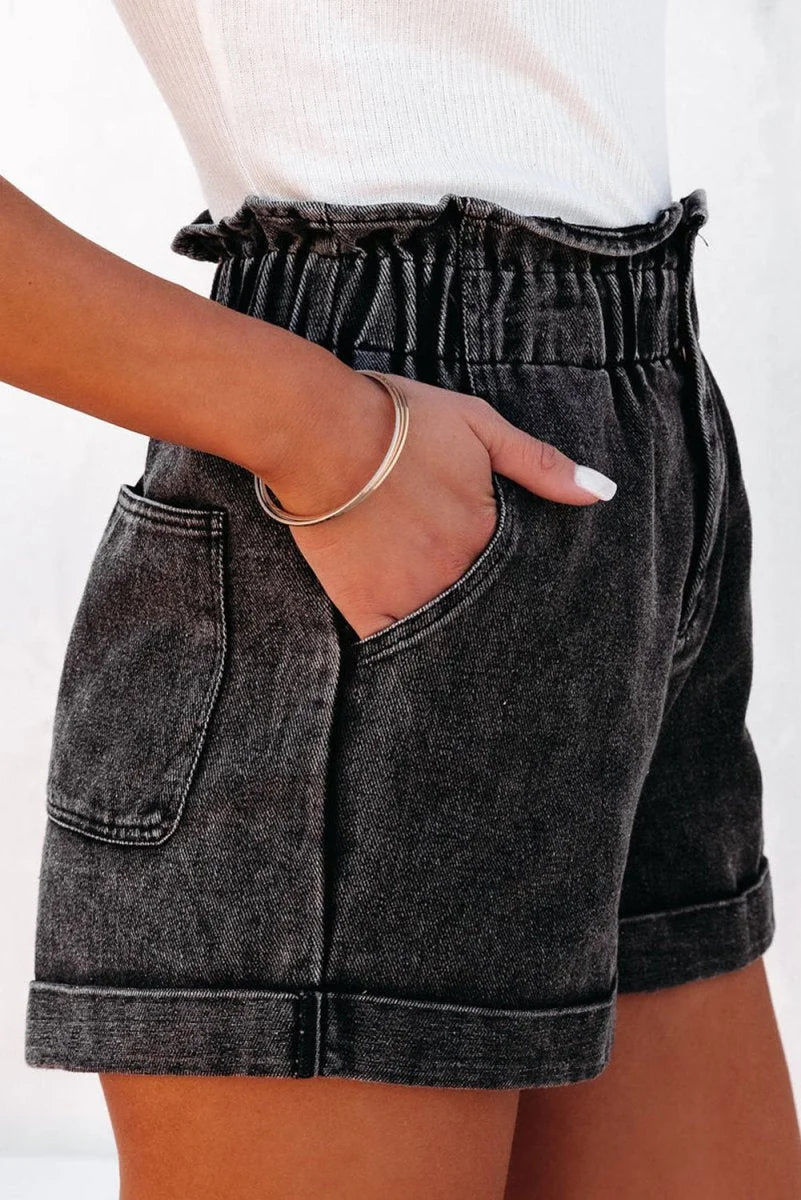 Close-up of black acid wash denim shorts with paperbag waist and cuffed hem.