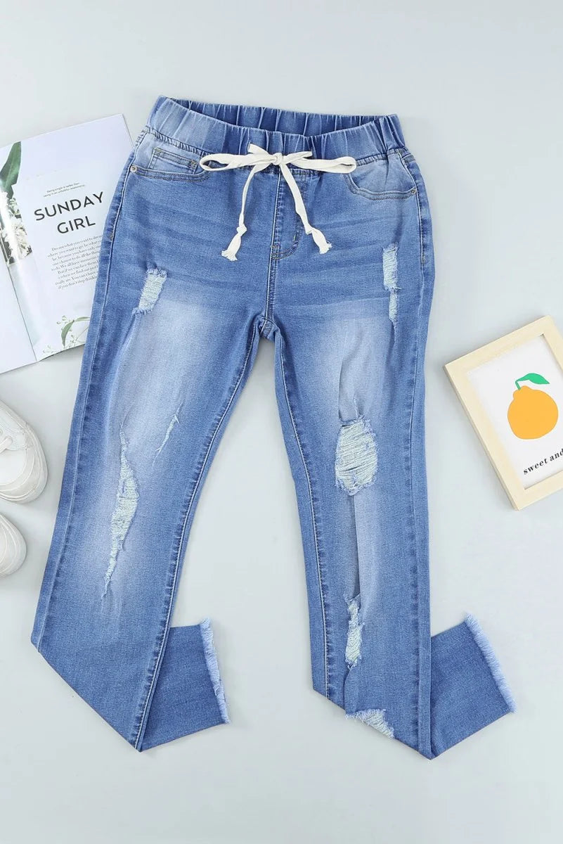 Light wash distressed denim jeans with a drawstring waist and frayed hem.