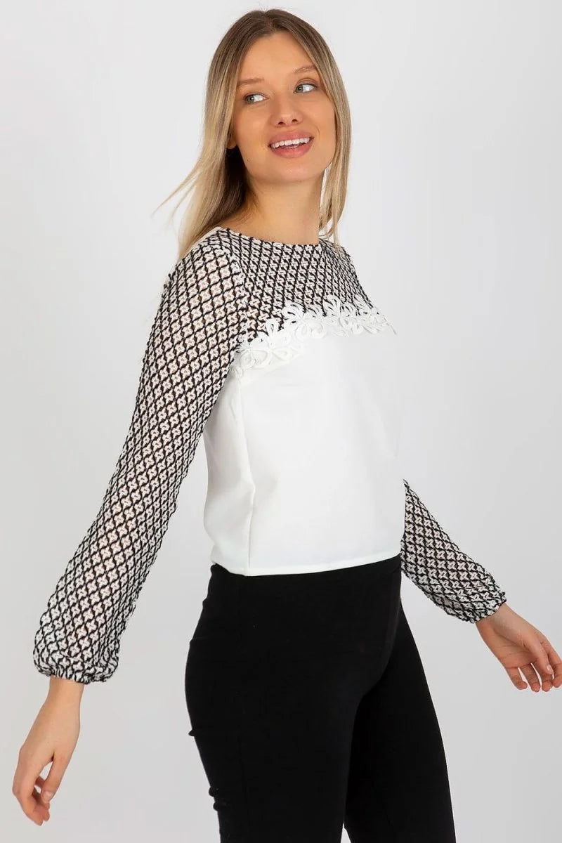 Woman wearing a white top with a black geometric print on the sleeves and a white lace trim.