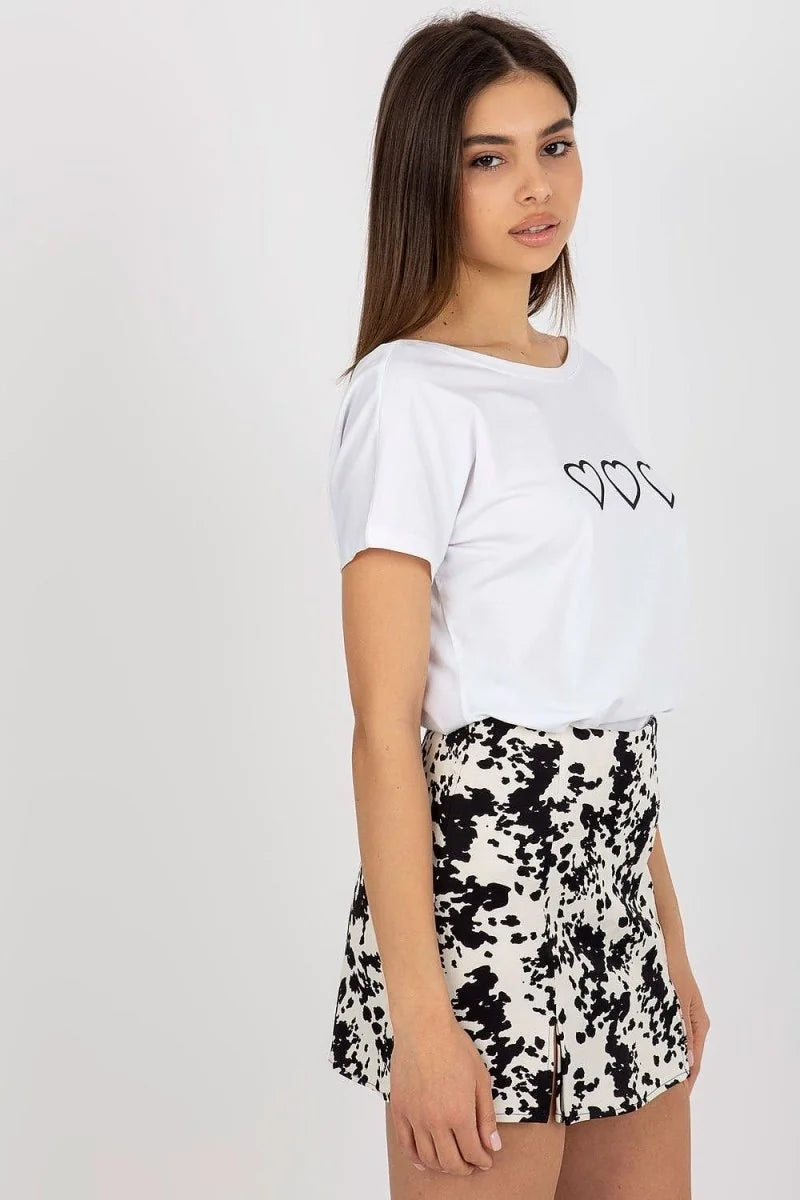 Woman in white t-shirt with black hearts and black and white patterned shorts.