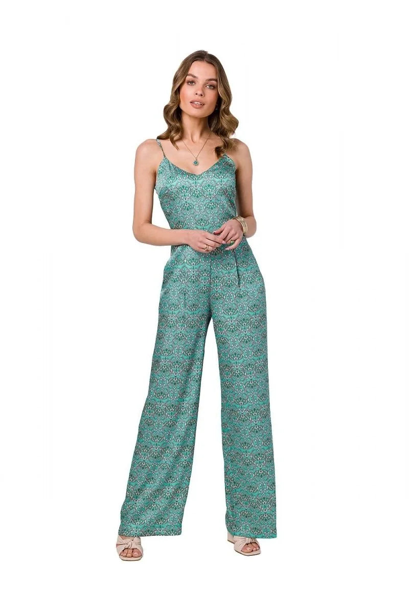 Woman in a teal jumpsuit with a delicate print, featuring a v-neck and wide legs, standing against a white background.