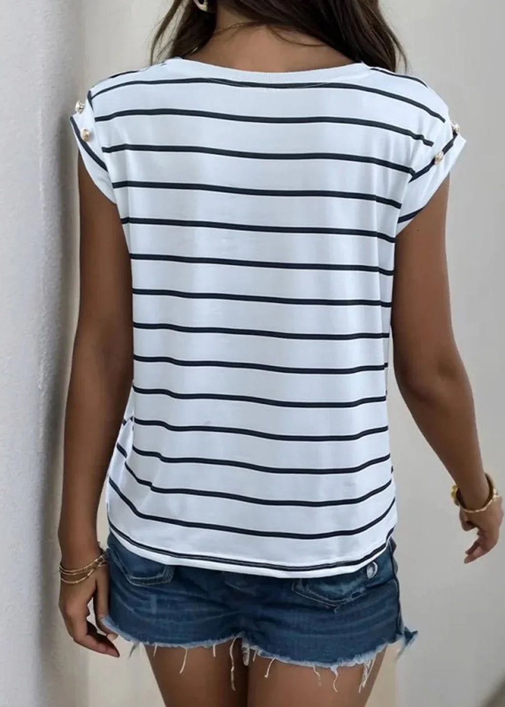 Back view of a white t-shirt with black stripes, cap sleeves, and gold button details, paired with denim shorts.