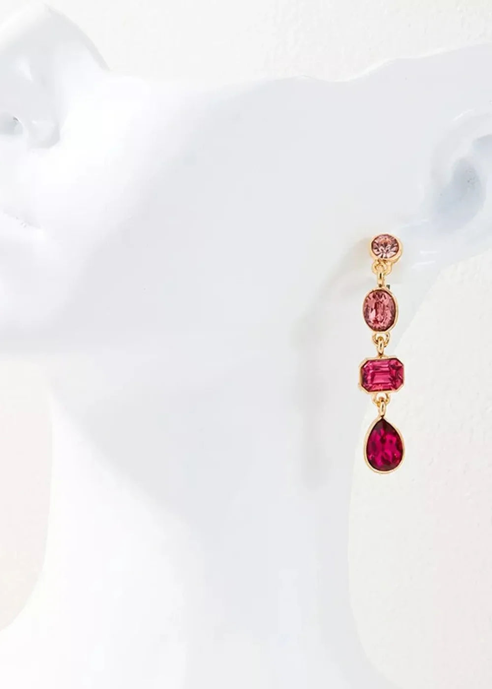 Dangling earring with a gold chain, featuring a round pink gem, an oval pink gem, a rectangular pink gem, and a teardrop p...