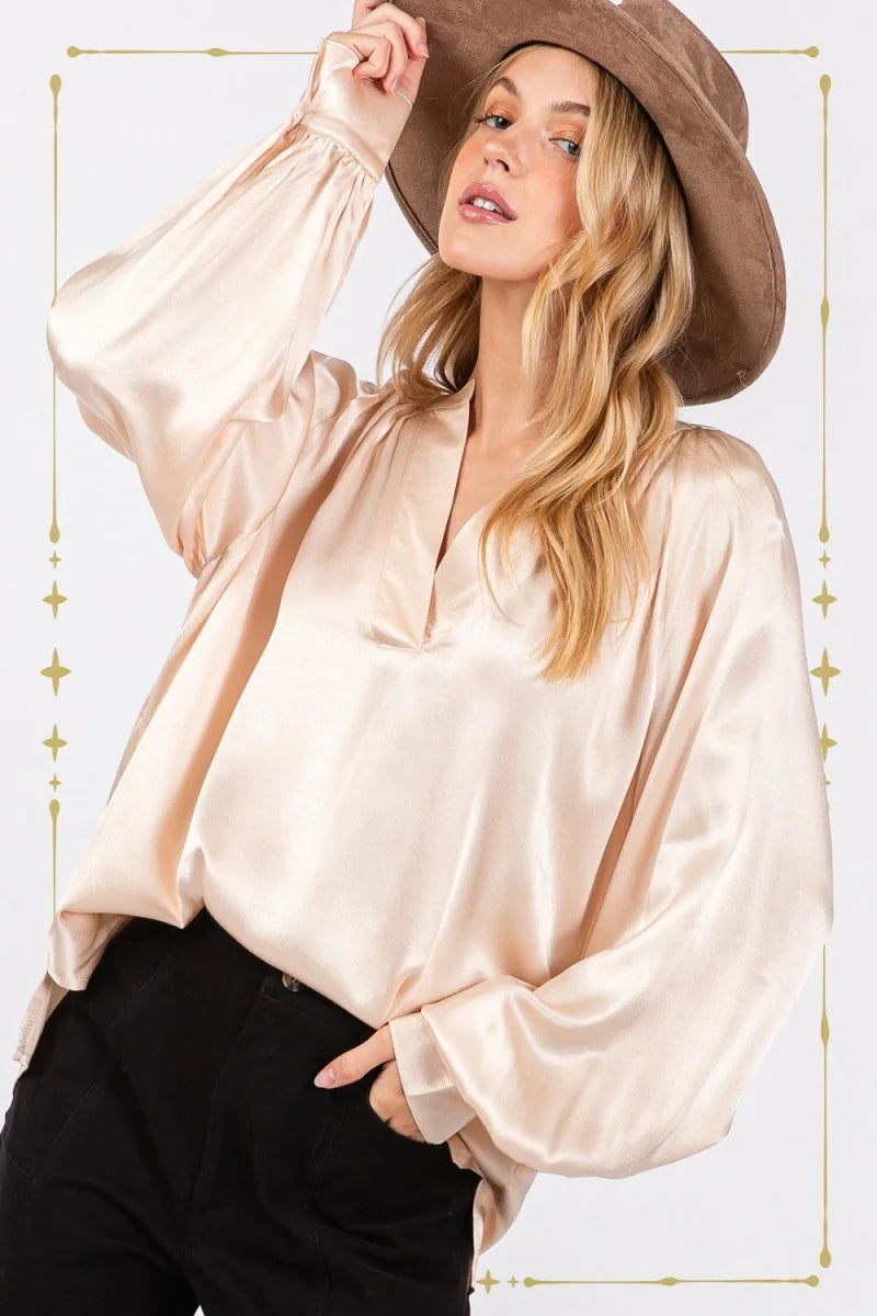 Relaxed fit champagne satin blouse with bishop sleeves and a v-neck, worn by a model with a brown hat.