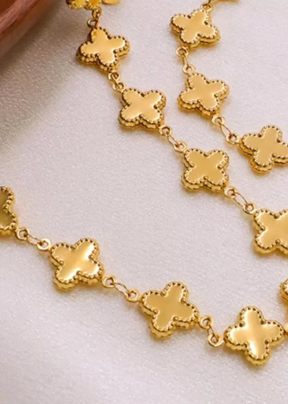 Gold-plated clover-shaped charms on a delicate chain bracelet with textured edges.