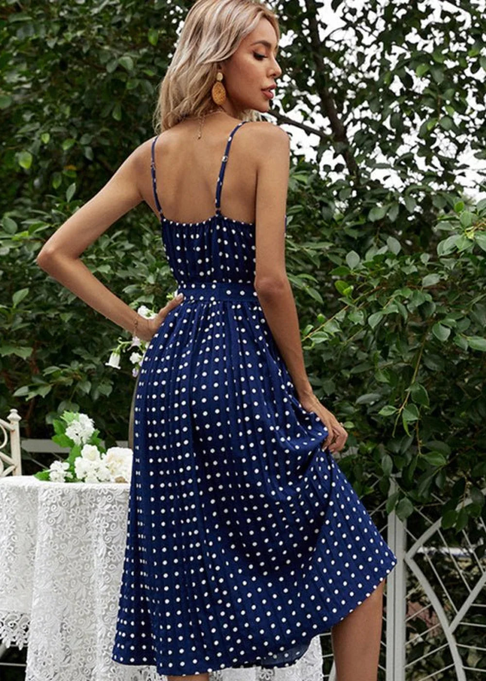 Navy blue polka dot midi dress with spaghetti straps and pleated skirt, seen from the side on a model.
