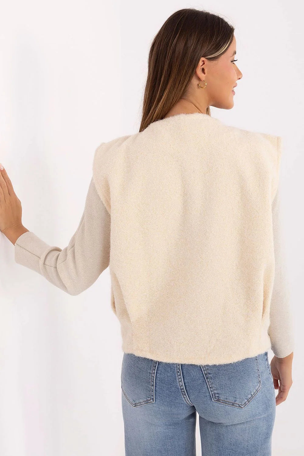 Back view of a cream textured knit vest over a long-sleeved shirt and blue jeans.
