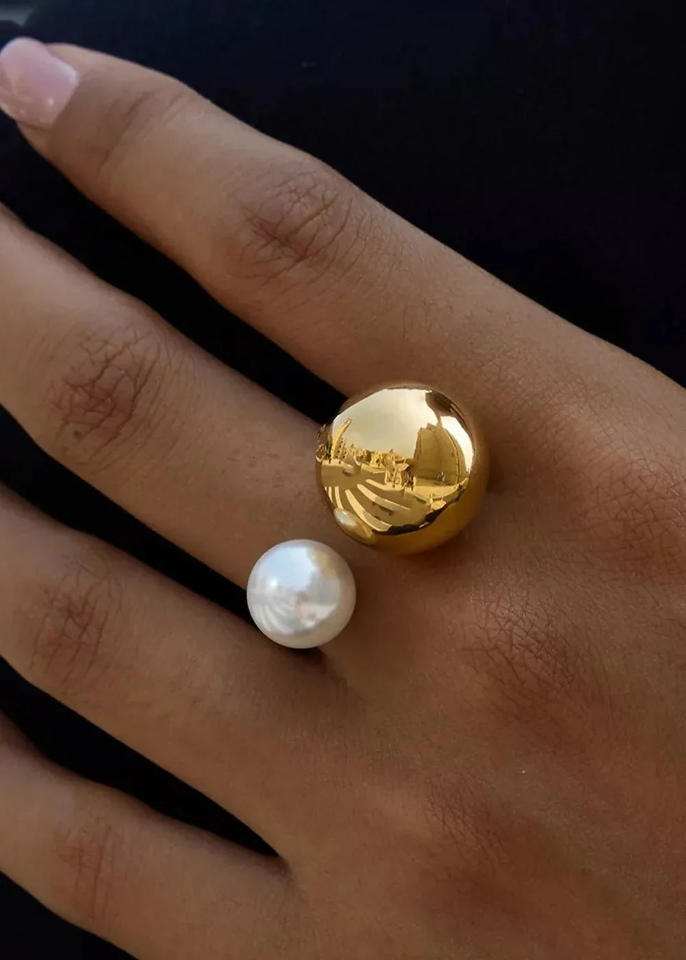 Gold orb and pearl ring on a hand with dark skin, reflecting a bright outdoor scene.