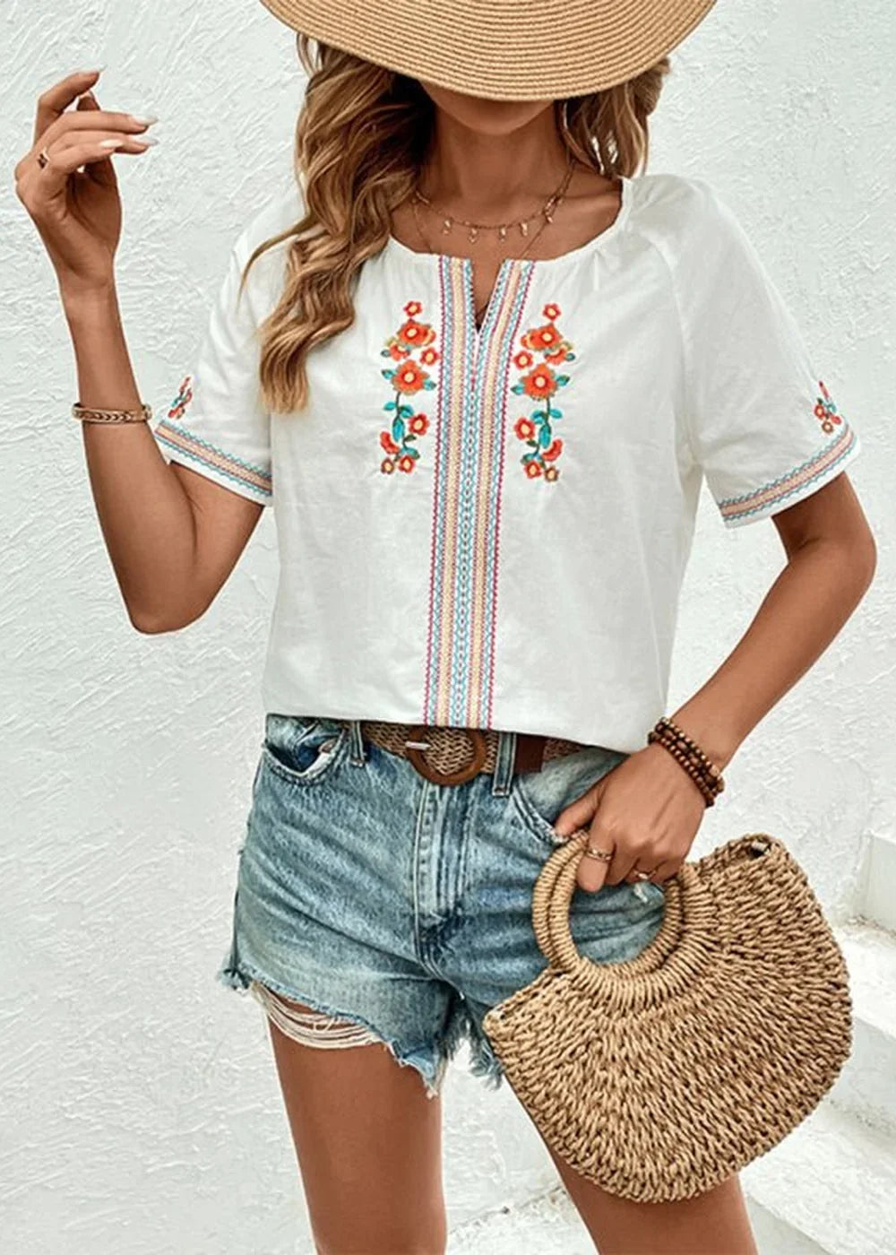 White embroidered boho top with colorful floral details and short sleeves, paired with distressed denim shorts.