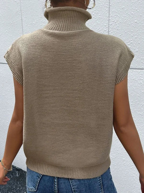 Back view of a woman wearing a tan, sleeveless, turtleneck knit sweater.