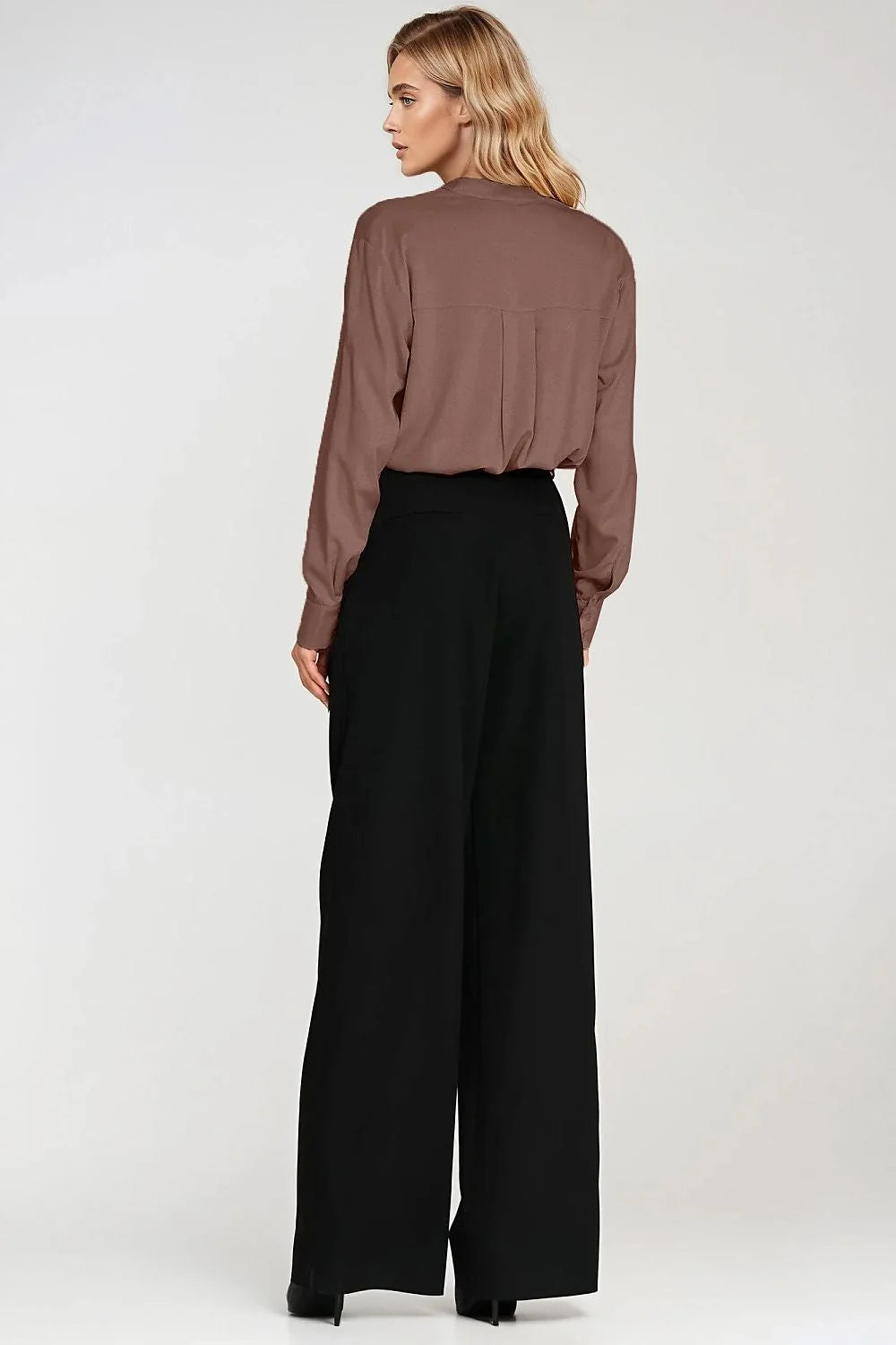 Back view of a woman wearing a brown long-sleeved collared shirt and black wide-leg pants.