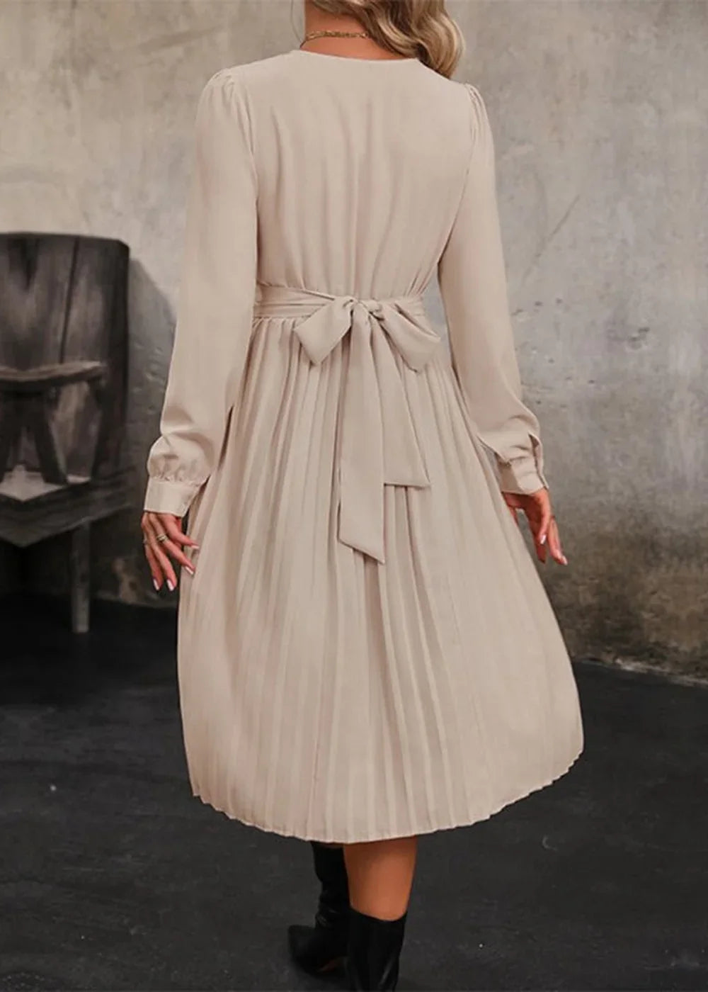 Beige long-sleeved pleated dress with a bow tie waist, shown from the back.