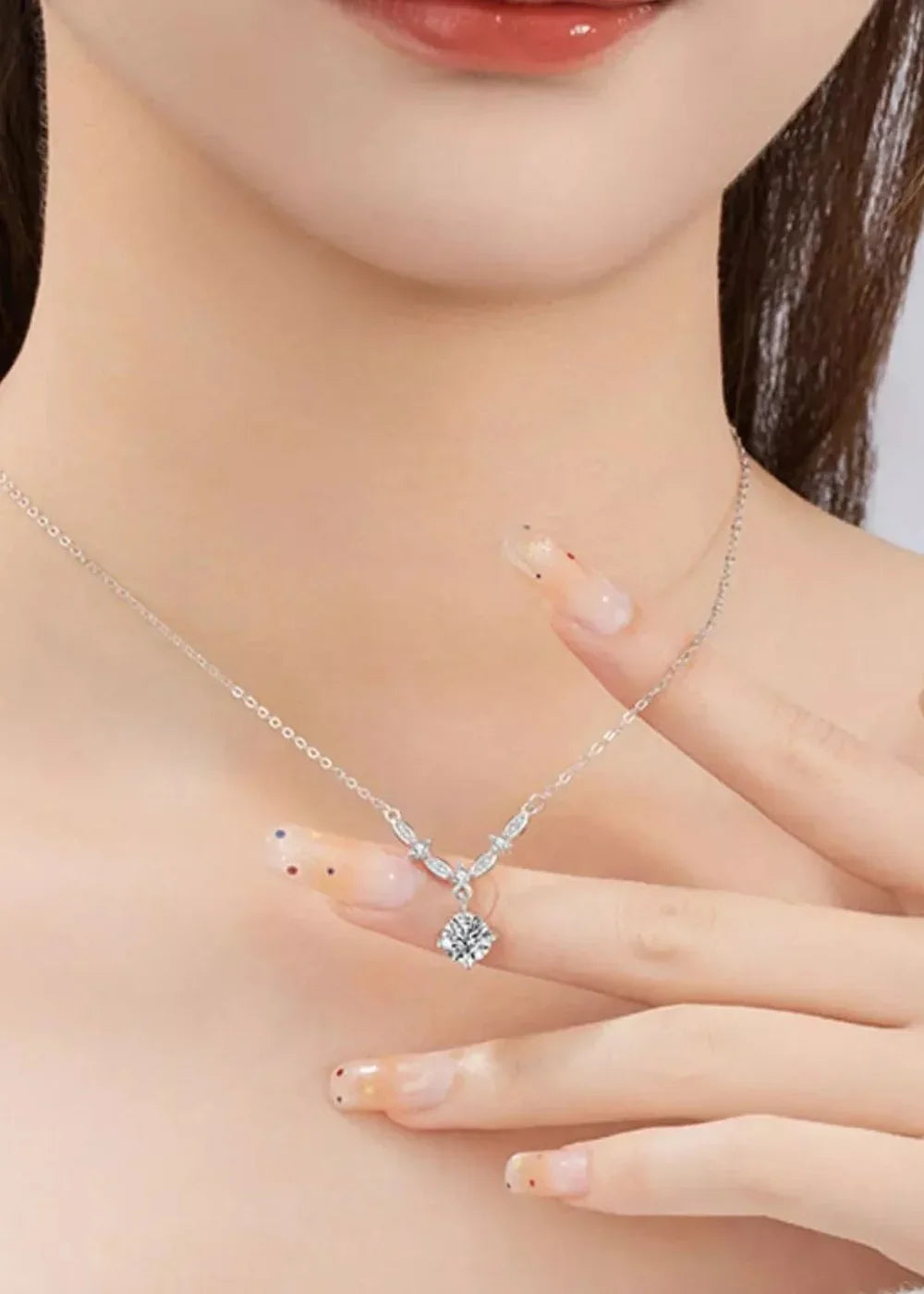 Close-up of a silver necklace with a diamond pendant on a woman's neck and chest.
