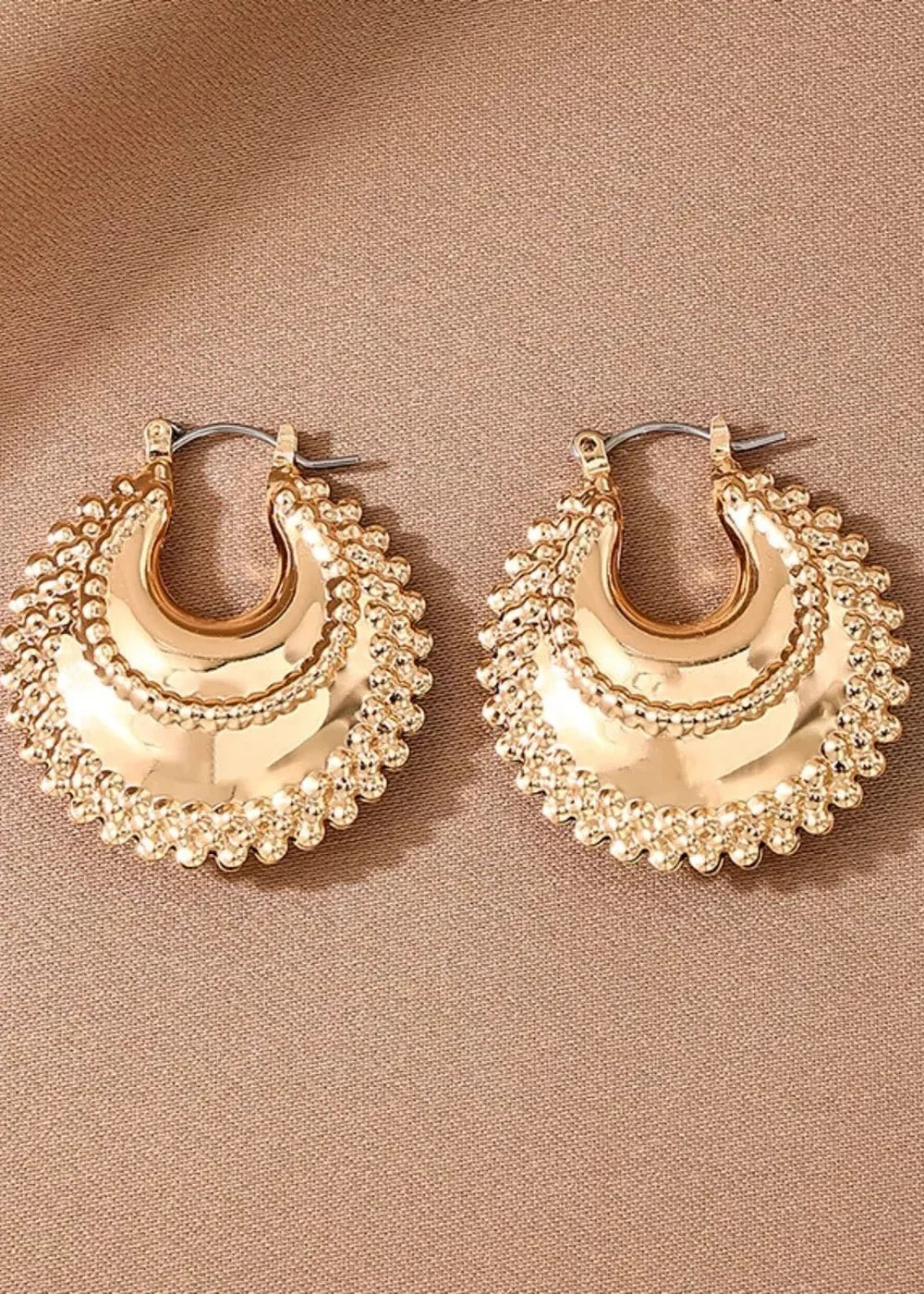Gold crescent hoop earrings with textured beaded edges on a taupe background.