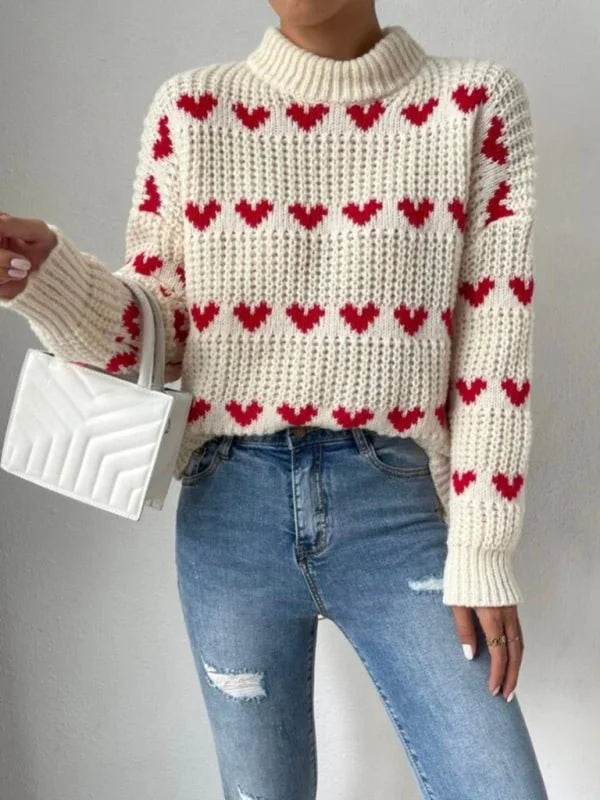 Cream knit sweater with red heart pattern and distressed blue jeans on model.