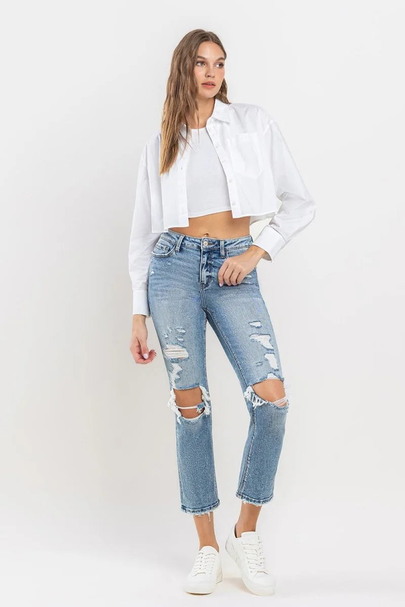 Light wash distressed denim jeans with ripped knees and frayed hem, on a model.