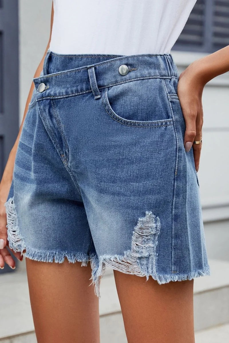 Distressed denim shorts with frayed hem and asymmetrical waist detail on model.