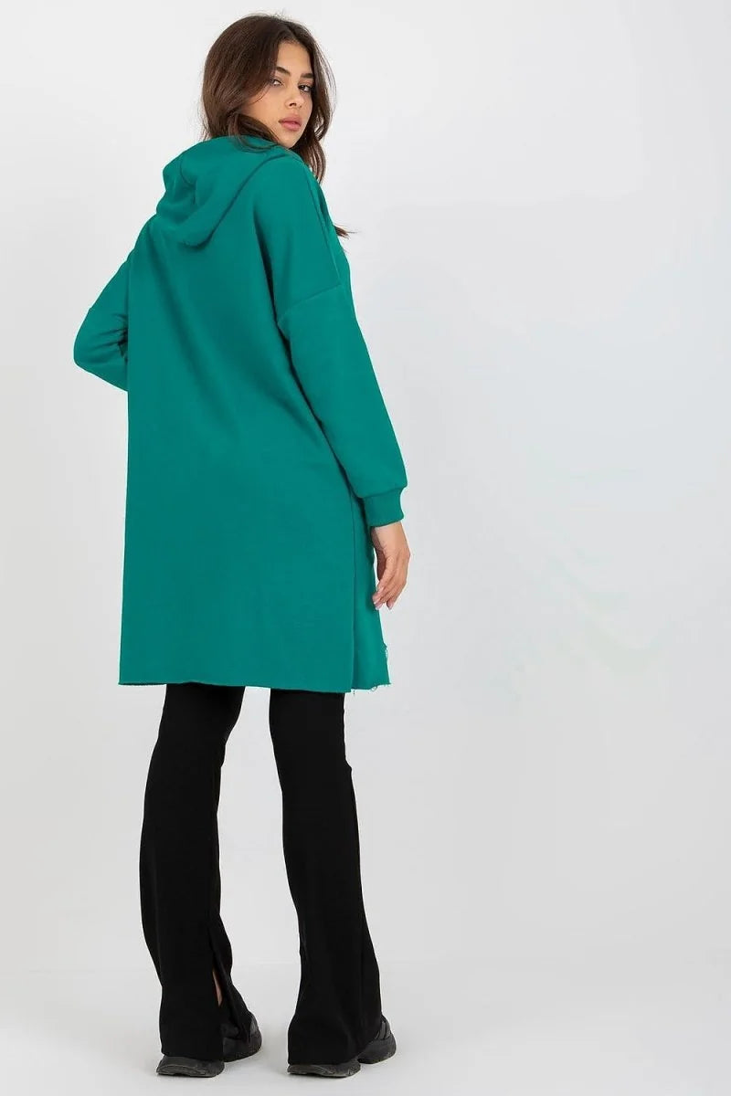 Woman in long teal hoodie with frayed hem and black flared pants, back view.