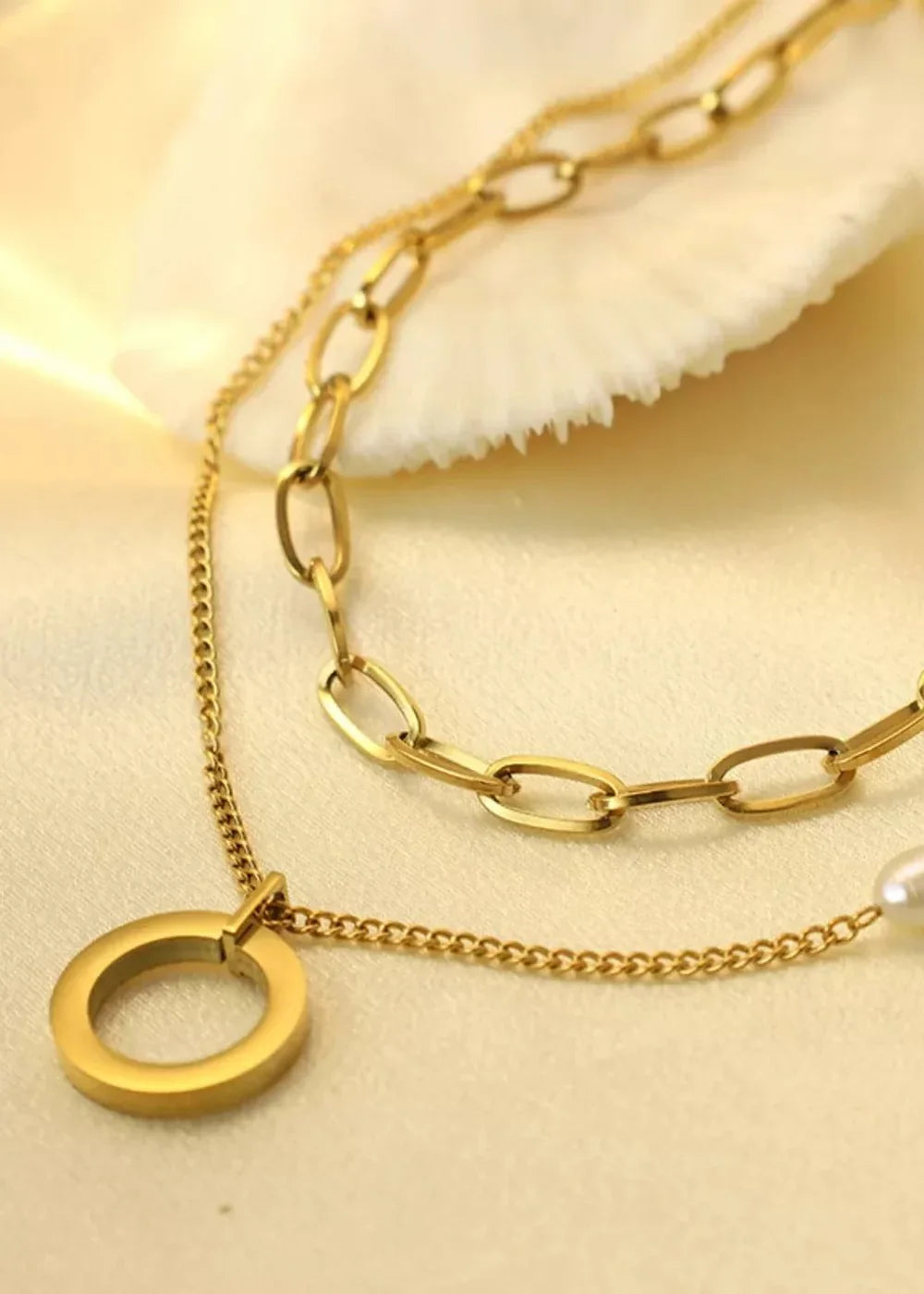 Close-up of a gold-plated layered necklace with a circle pendant and a pearl.