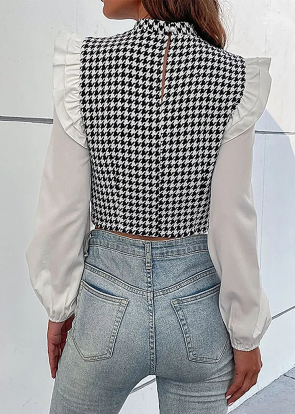 Back view of a black and white houndstooth crop top with white ruffled sleeves and light wash jeans.