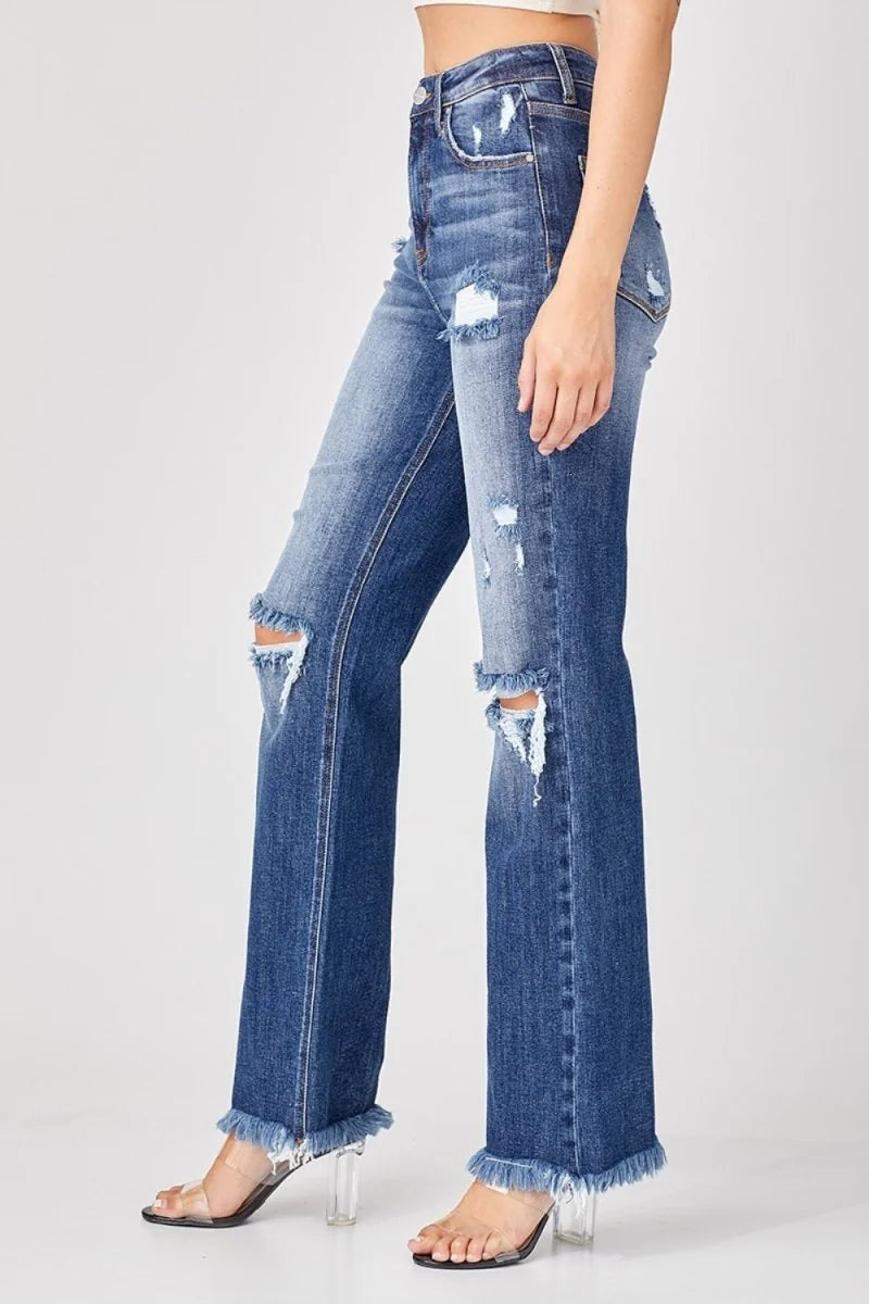 Distressed blue denim jeans with a frayed hem and a straight fit, shown on a model.
