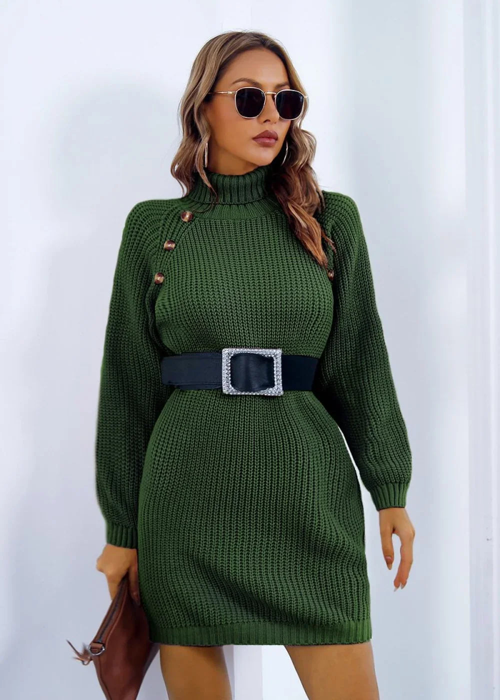 Model in a dark green ribbed knit turtleneck sweater dress cinched with a black belt with a square buckle.