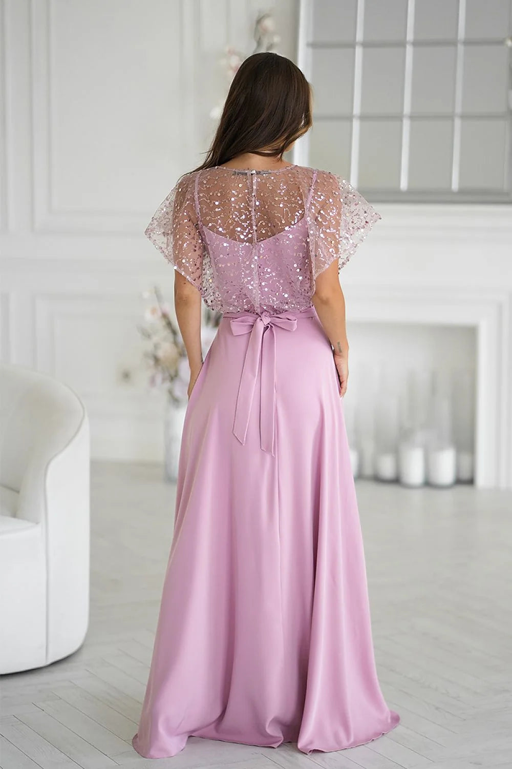 Back view of a lilac maxi dress with a sparkling sequined overlay and a satin bow at the waist.