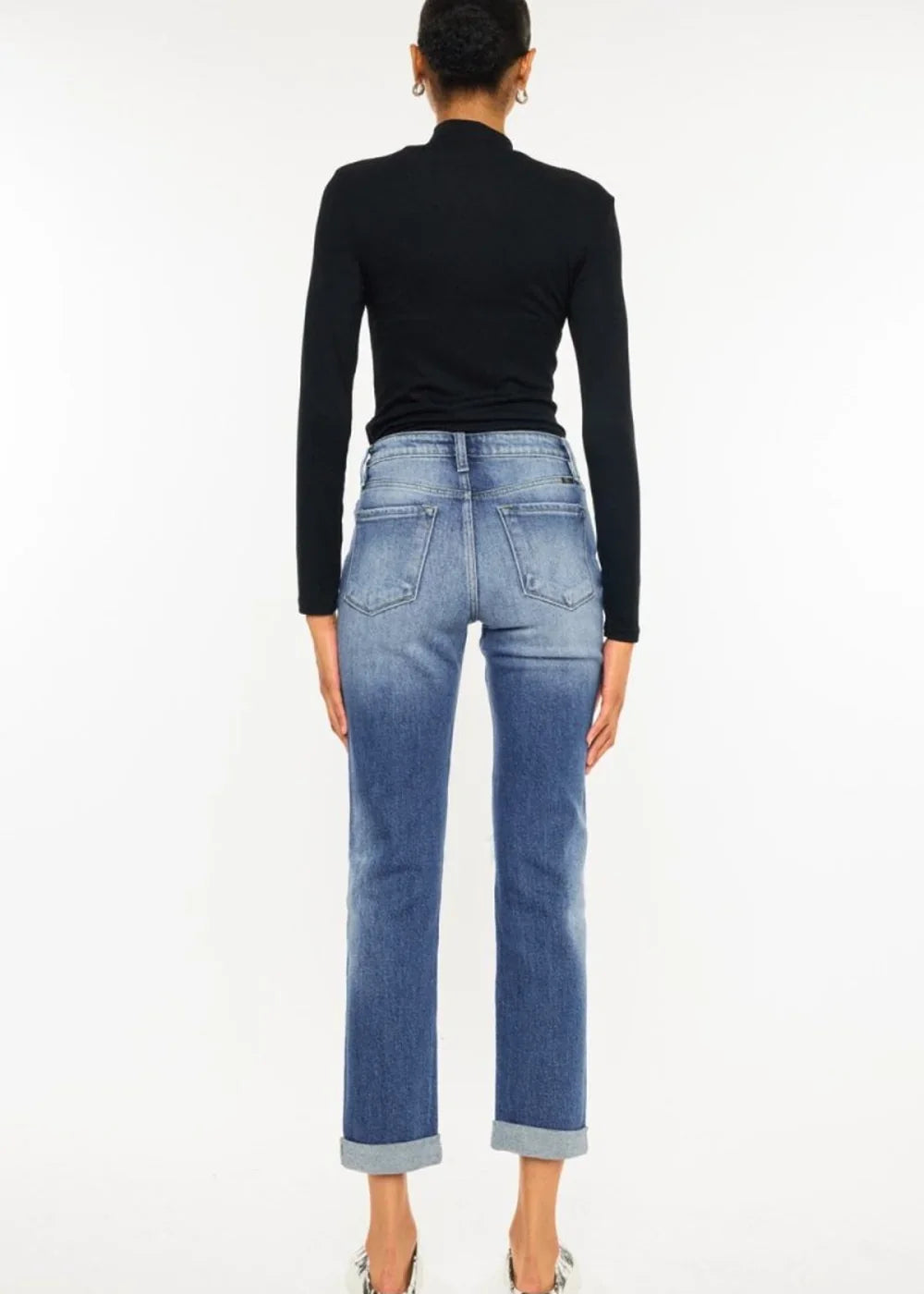 Back view of a woman in a black mock neck top and distressed light wash denim jeans with cuffed hems.
