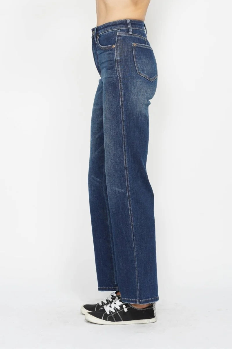 Side view of a model wearing dark wash, straight-leg jeans with a subtle distressed texture, paired with black and white s...