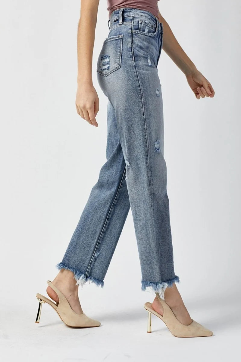 Light wash distressed denim jeans with frayed hem, shown on a model.