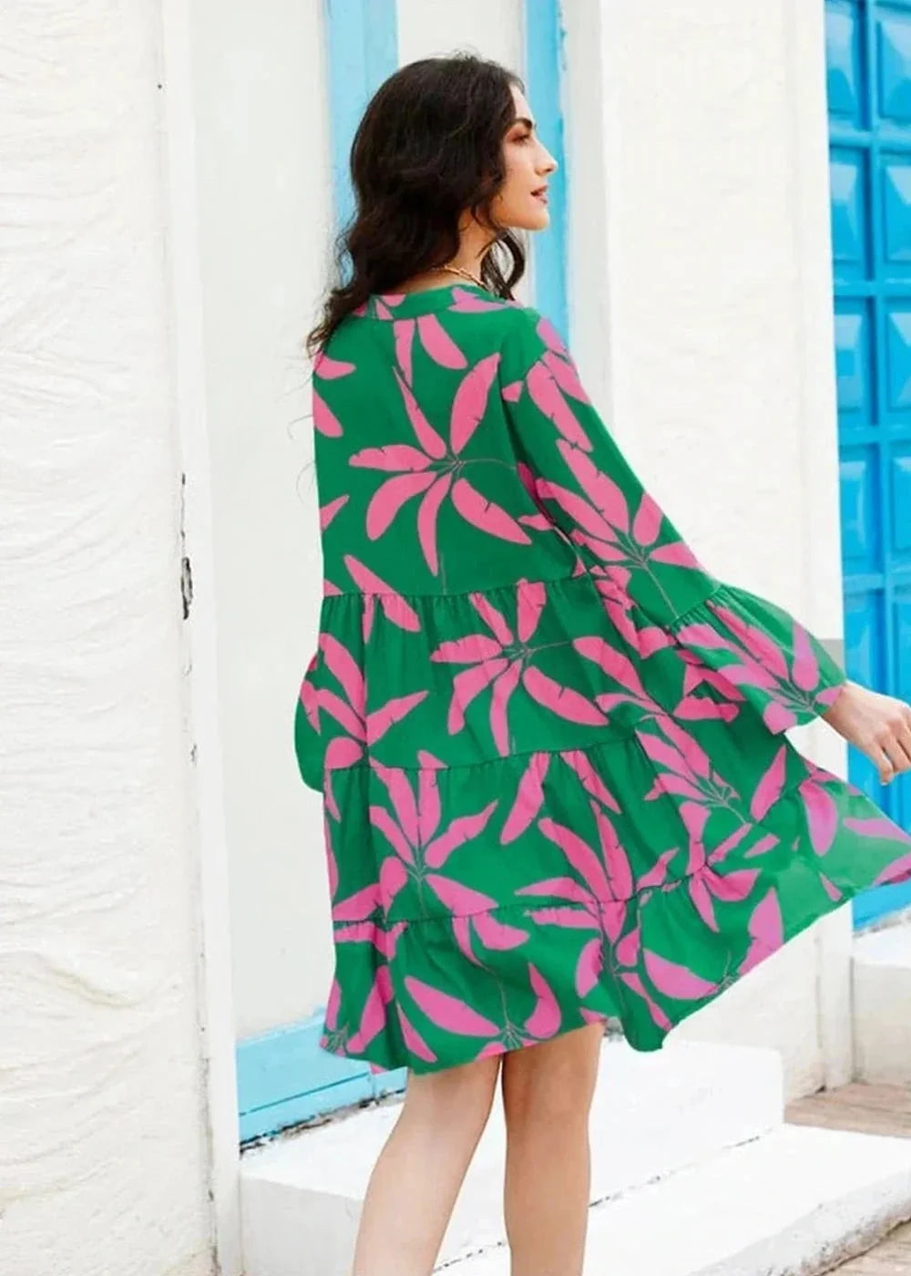 Green tiered mini dress with a bold pink tropical leaf print, featuring long bell sleeves.
