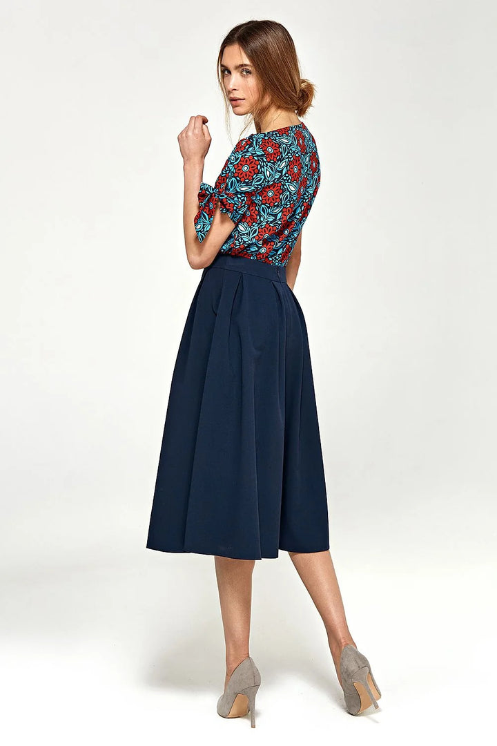 Navy blue midi skirt with pleats on a model wearing a floral print top and grey heels.
