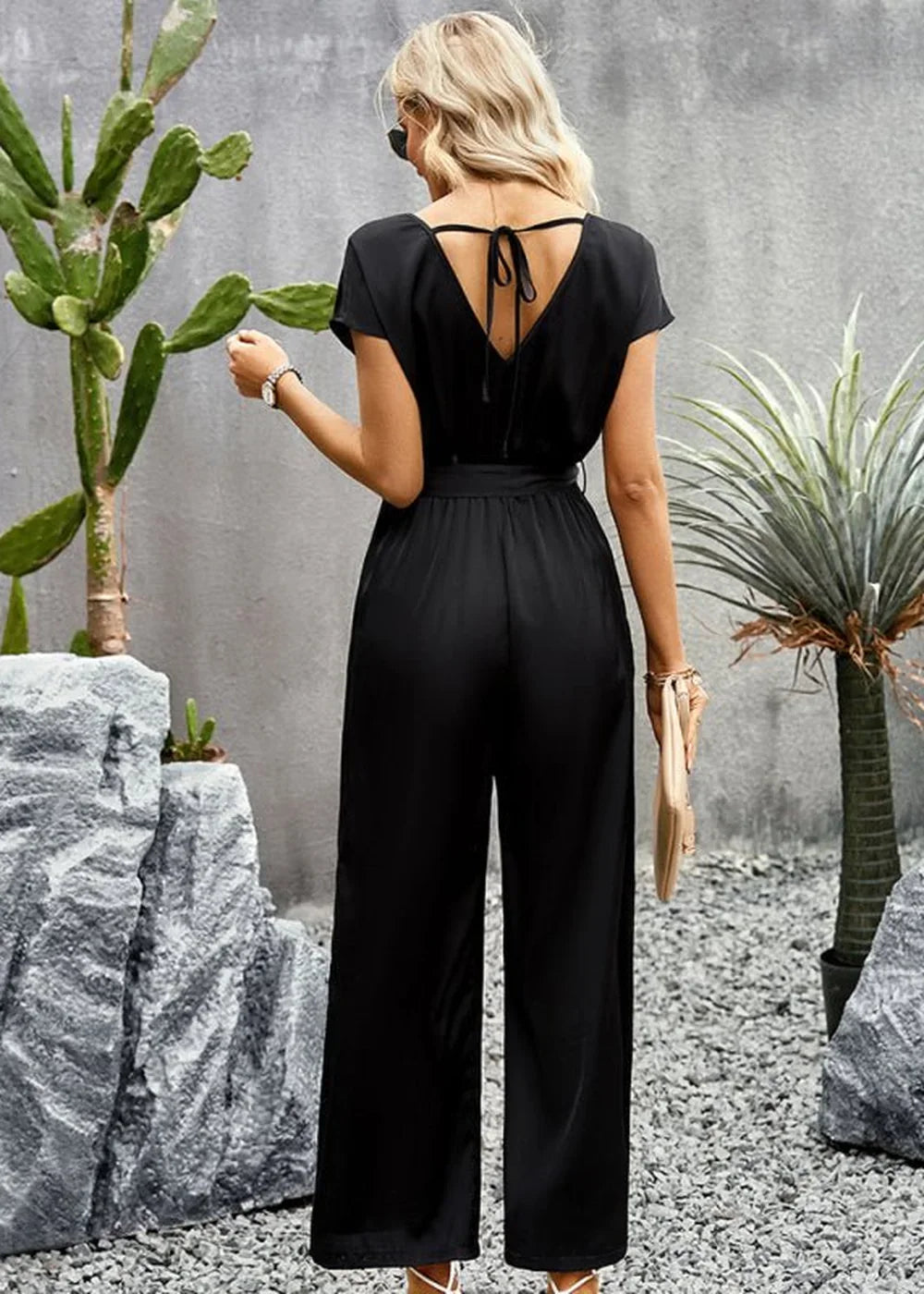Back view of a woman wearing a black wide-leg jumpsuit with a tie-back V-neck and a belted waist.
