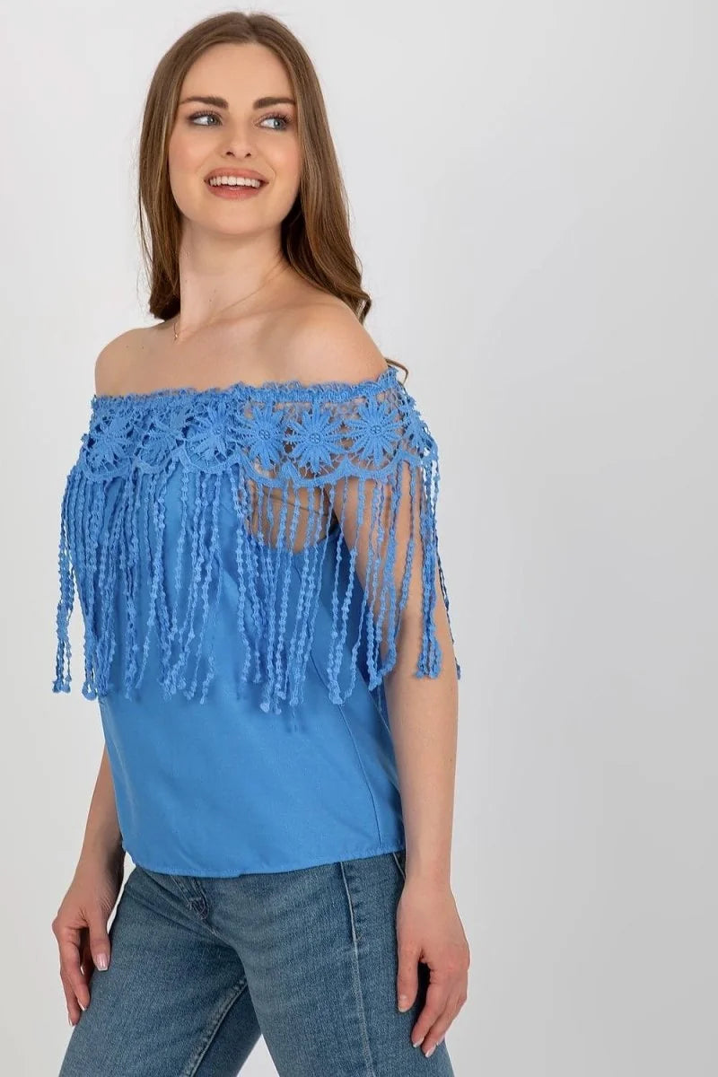 Off-the-shoulder blue top with intricate crochet detailing and fringe accents, worn by a model.